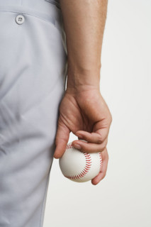 Close up of man holding baseball at side.