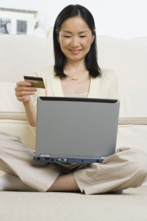 Asian woman with credit card sitting on floor using laptop .
