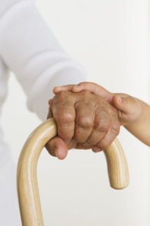 Child's hand laying hand of senior holding cane.