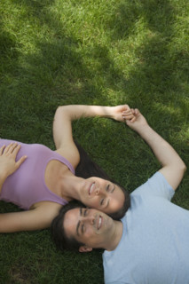 Couple laying with heads together on grass.