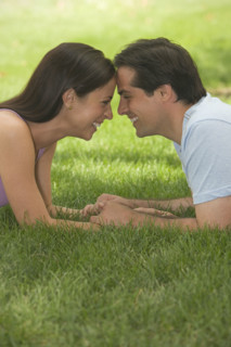 Couple touching foreheads and smiling in grass.