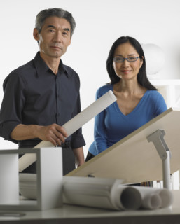 Asian businessman and businesswoman at drafting table with blueprints.