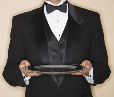 Waiter in tuxedo holding silver platter.