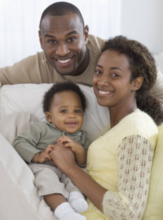 Portrait of parents and baby on sofa.
