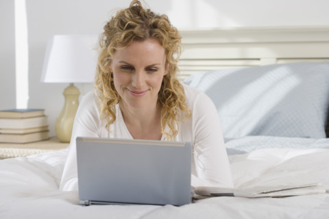 Woman looking at laptop on bed.