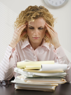 Businesswoman rubbing temples and looking at paperwork.