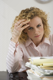 Businesswoman rubbing temple and looking at paperwork.