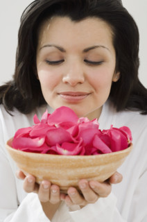 Woman smelling bowl of flower petals.