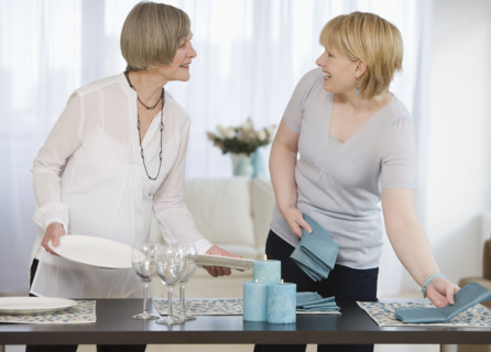 Mother and adult daughter setting table.