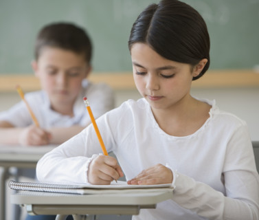 Girl writing at desk in classroom.