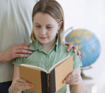 Girl reading book next to father.