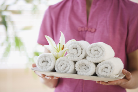 Woman holding tray of rolled towels.
