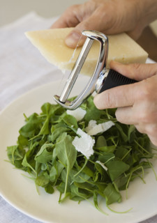 Man shaving cheese onto salad.