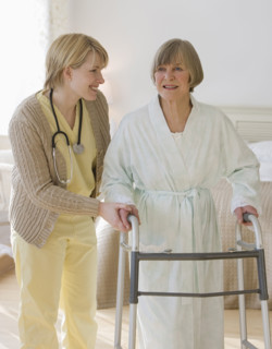 Nurse helping senior woman use walker.
