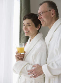 Couple in bathrobes looking out window.