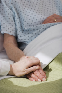 Nurse holding senior woman’s hand in hospital.