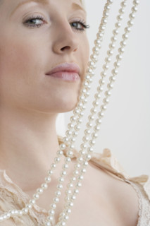 Woman with pearl necklace against face.