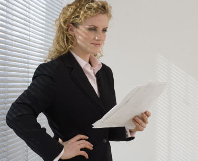 Businesswoman reading paperwork next to window.