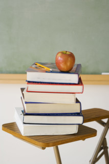 Stack of books and apple in classroom.