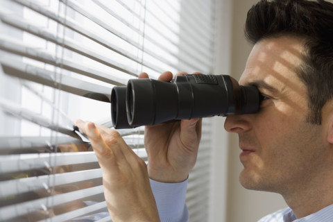 Businessman looking out window through binoculars.