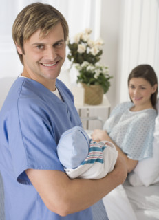 Portrait of father holding newborn baby in hospital.