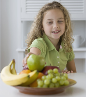 Girl reaching for fruit in bowl.