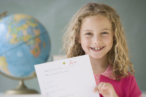 Girl holding up A plus paper in classroom.