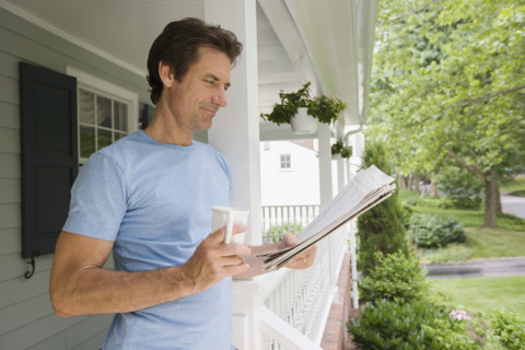 Man reading newspaper on porch.