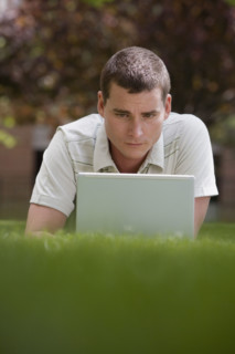 Man using laptop in grass.