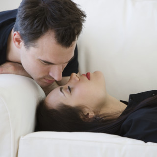 Man leaning over girlfriend on sofa.