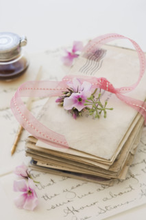 Stack of old letters next to flowers and ink bottle.