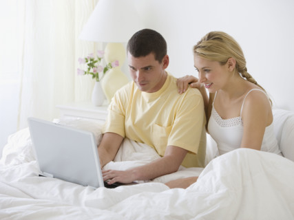Couple looking at laptop in bed.