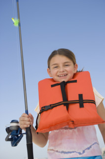 Girl in life jacket holding fishing pole.