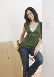 Woman leaning on wall with hammer and level indoors. Date : 2006