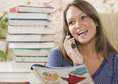 Young woman using cell phone next to stack of books. Date : 2006