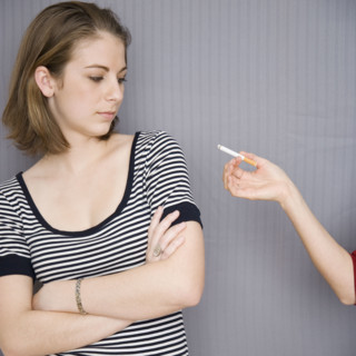 Teenage girl looking at cigarette in friend’s hand. Date : 2007