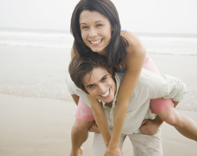 Man giving woman piggyback ride at beach. Date : 2006