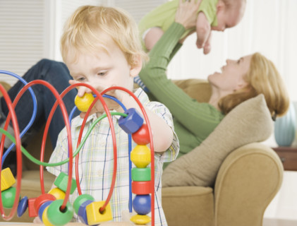 Young son playing with block toy with mother and baby in background. Date : 2006