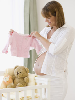 Pregnant woman holding up baby clothing. Date : 2007