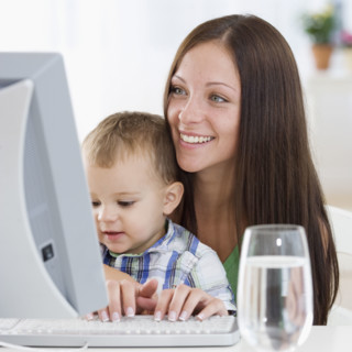 Mother holding baby and typing on computer. Date : 2007