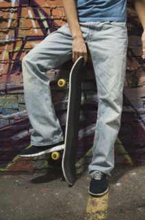 Asian man holding skateboard in front of graffitied wall. Date : 2007
