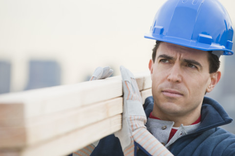 Male construction worker holding stack of lumber.