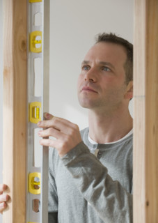 Man holding level next to wooden stud.
