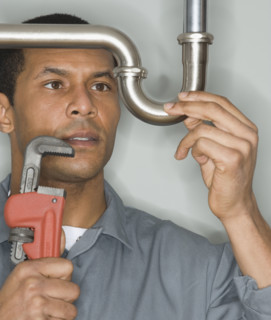 African male plumber holding wrench next to pipe.