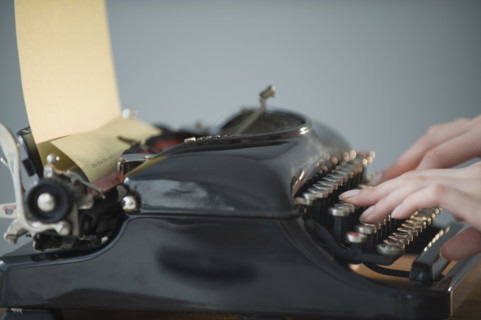 Woman typing on antique typewriter.