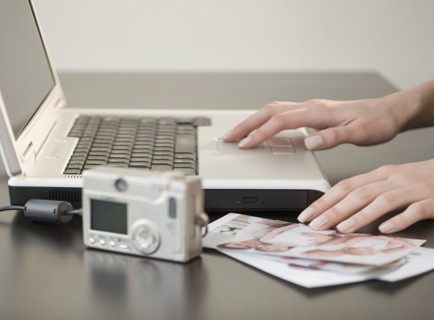 Digital camera and photographs next to laptop.