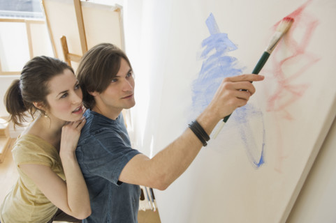 Woman watching boyfriend paint on easel.