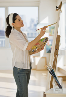 Hispanic woman painting on easel.
