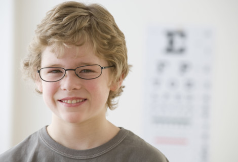 Boy wearing eyeglasses in front of eye chart.