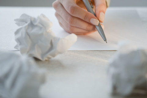 Woman writing next to crumpled papers.